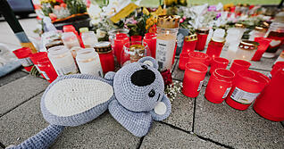 Blumen und Kerzen liegen auf einem Parkplatz eines Supermarktes in der Criesbacher Straße. Ein 18-Jähriger soll einen zwölfjährigen Jungen am Donnerstagabend in der kleinen Gemeinde Niedernhall nach einem Streit auf dem Parkplatz mit dem Auto verfolgt und absichtlich auf seinem Fahrrad angefahren haben. Das Kind starb noch vor Ort.