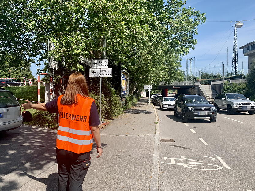 Eine Helferin von der Feuerwehr zeigt den Autos den Weg in die Drive-In-Impftstraße. Die Warteschlange der Autos verläuft bis zum Club Hip Hisland in der Hafenstraße.