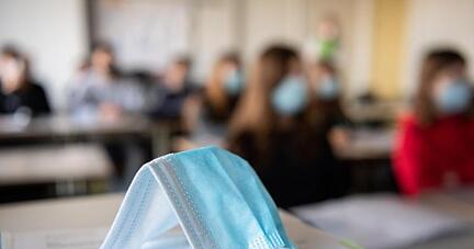 Eine Maske liegt im Unterricht auf Unterlagen.