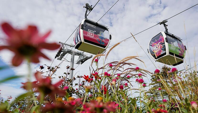 Kabinen der Seilbahn schweben auf dem Gelände der Bundesgartenschau über eine Blumenwiese. Kabinen der Seilbahn schweben auf dem Gelände der Bundesgartenschau über eine Blumenwiese.