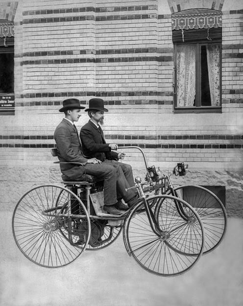 Wilhelm Maybach am Steuer des von ihm 1889 konstruierten Stahlradwagens, neben ihm Adolf Daimler. Bei diesem Wagen verließ Maybach die Form der Pferdekutsche. Es ist auch das erste Fahrzeug mit Viergang-Zahnradgetriebe. Das Kühlwasser durchfließt die Stahlrohre des Fahrgestells.