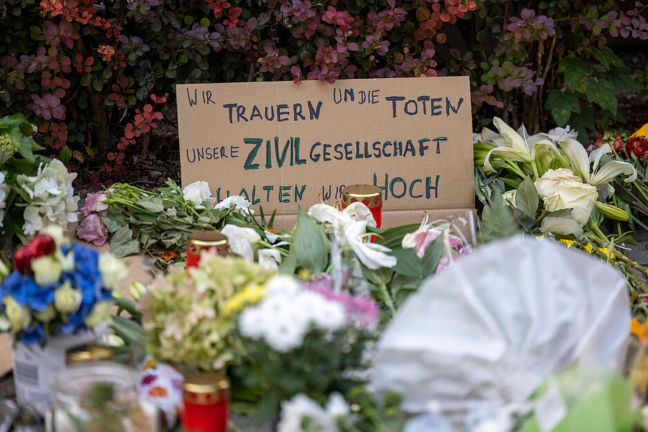 In der Nähe des Tatorts haben Menschen Blumen, Kerzen und auf Schildern gemalte Botschaften niedergelegt. Auf einem Schild steht "Wir trauern um die Toten - Unsere Zivilgesellschaft halten wir hoch".