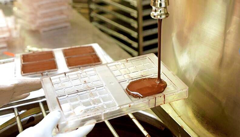 Ein Mitarbeiter fängt die flüssige Schokolade aus dem Temperiergerät in Formen auf. Ein Mitarbeiter fängt die flüssige Schokolade aus dem Temperiergerät in Formen auf.