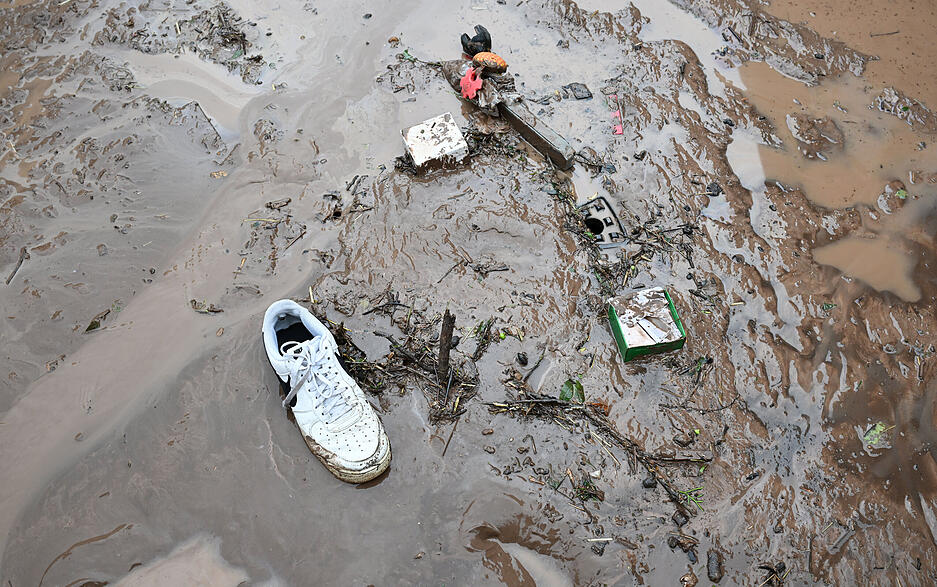 Auf einer nach einem Unwetter verschlammten Straße liegt ein weggespülter Turnschuh. Auf einer nach einem Unwetter verschlammten Straße liegt ein weggespülter Turnschuh.