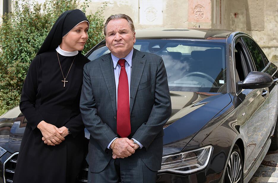 Janina Hartwig, als Schwester Hanna, und Fritz Wepper, als Bürgermeister Wolfgang Wöller, stehen in einer Szene der ARD-Serie "Um Himmels Willen" vor einem Auto.