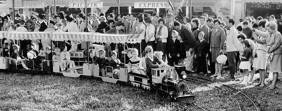 Mit dem Pacifik-Express fahren kleine Volksfestgäste begeistert mit. Eltern, Großeltern und Geschwister schauen zu und winken. Aufnahme aus den 1960er Jahren.