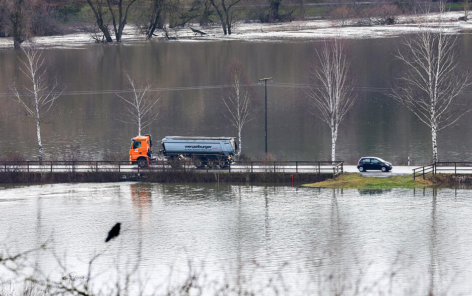 Fahrzeuge fahren in Riedlingen zwischen den Ortsteilen Zell und Bechingen auf einer Straße zwischen überfluteten Wiesen. Im oberen Bildrand fließt die Donau. Die Hochwasserlage bleibt in Teilen Baden-Württembergs weiterhin angespannt.