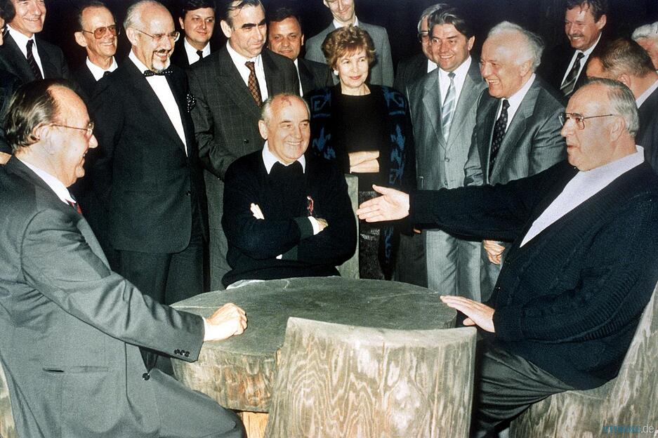Bundeskanzler Helmut Kohl, der sowjetische Staatspr&auml;sident Michail Gorbatschow (Mitte) und Bundesau&szlig;enminister Hans-Dietrich Genscher (links) unterhalten sich am 15.07.1990 an einem rustikalen Arbeitstisch im Garten von Gorbatschows G&auml;stehaus in Archys, Russland, 2.v.r. Au&szlig;enminister Eduard Schewardnadse. In der Mitte hinten Raissa Gorbatschowa, daneben Finanzminister Theo Waigel. Foto: Archiv/Roberto Pfeil/dpa