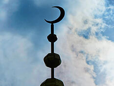 Der Halbmond auf dem Minarett einer Moschee hebt sich am als Schattenriss vor Wolken ab. (Symbolbild)