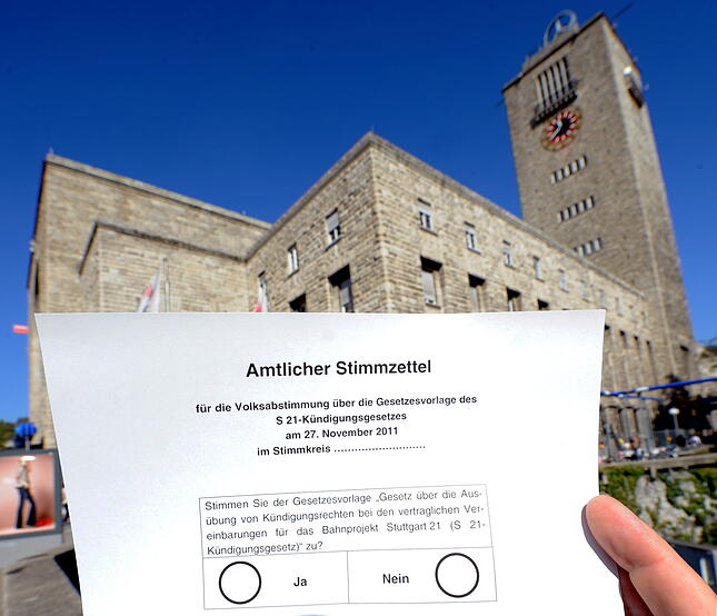 ARCHIV - ILLUSTRATION - Eine Hand hält einen Stimmzettel zur Volksabstimmung über das umstrittene Bahnprojekt Stuttgart 21 vor den Hauptbahnhof in Stuttgart, aufgenommen am 30.09.2011. Gut sechs Wochen vor der Volksabstimmung zu Stuttgart 21 hat Ministerpräsident Winfried Kretschmann (Grüne) ein Ende der erbitterten Grabenkämpfe gefordert. «Jetzt geht es in die Sachauseinandersetzung», sagte der Grünen-Politiker im Stuttgarter Landtag. Foto: Bernd Weißbrod dpa/lsw (zu lsw 1007 vom 13.10.2011) +++ dpa-Bildfunk +++ ARCHIV - ILLUSTRATION - Eine Hand hält einen Stimmzettel zur Volksabstimmung über das umstrittene Bahnprojekt Stuttgart 21 vor den Hauptbahnhof in Stuttgart, aufgenommen am 30.09.2011. Gut sechs Wochen vor der Volksabstimmung zu Stuttgart 21 hat Ministerpräsident Winfried Kretschmann (Grüne) ein Ende der erbitterten Grabenkämpfe gefordert. «Jetzt geht es in die Sachauseinandersetzung», sagte der Grünen-Politiker im Stuttgarter Landtag. Foto: Bernd Weißbrod dpa/lsw (zu lsw 1007 vom 13.10.2011) +++ dpa-Bildfunk +++