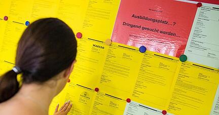 Eine junge Frau blickt auf eine Aush&auml;ngewand mit Zetteln f&uuml;r freie Ausbildungsstellen.