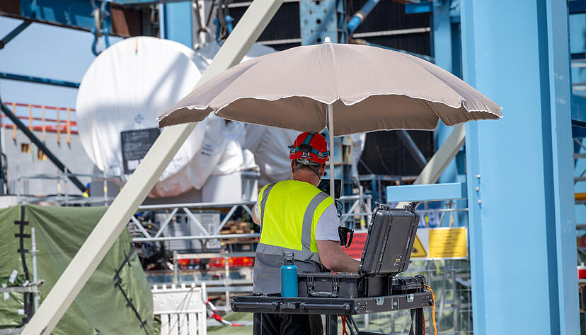 Geschützt durch einen Schirm vor der Sonne arbeitet ein Mann auf der EnBW-Baustelle am Einbau der Turbine.