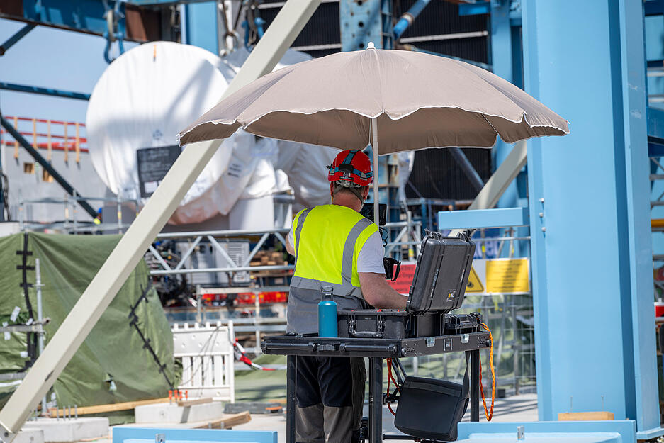Geschützt durch einen Schirm vor der Sonne arbeitet ein Mann auf der EnBW-Baustelle am Einbau der Turbine.