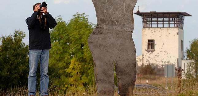 Am einstigen DDR-Grenzübergang Henneberg-Eußenhausen bei Meiningen (Thüringen) wird eine Skulptur am Dienstag (27.09.2005) von einem jungen Mann fotografiert. Sie ist aus zwei Zentimeter dickem Stahlblech gefertigt und zeigt einen Menschen, der in die Knie sinkt, nachdem er auf der Flucht an der einstigen innerdeutschen Grenze erschossen wurde. Die mehr als vier Meter hohe Skulptur, aufgestellt in Sichtweite eines ehemaligen Wachturms der DDR-Grenzposten, wurde vom Berliner Aktionskünstler Jimmy Fell geschaffen. Offiziell wird die neue Figur im Skulpturenpark auf der früheren Grenze am 3. Oktober, den Tag der Deutschen Einheit, in einer Feierstunde übergeben. Foto: Martin Schutt dpa/lth +++(c) dpa - Bildfunk+++ | Verwendung weltweit