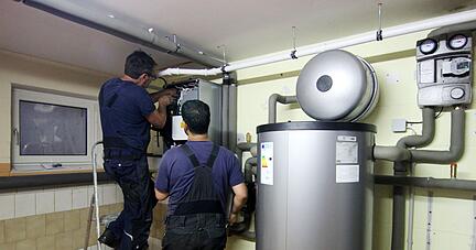 Zwei Handwerker stellen eine gerade installierte Wärmepumpe im Keller einer Doppelhaushälfte ein.