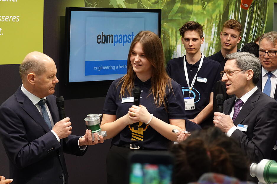 Bundeskanzler Olaf Scholz l&auml;sst sich von EBM-Papst-Studentin Melanie Bildhoff erl&auml;utern, was das Besondere an den Kompressoren ist. Rechts EBM-Papst-Chef Klaus Gei&szlig;d&ouml;rfer.