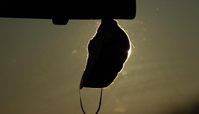 Eine FFP2-Maske hängt vor der aufgehenden Sonne in einem Auto.