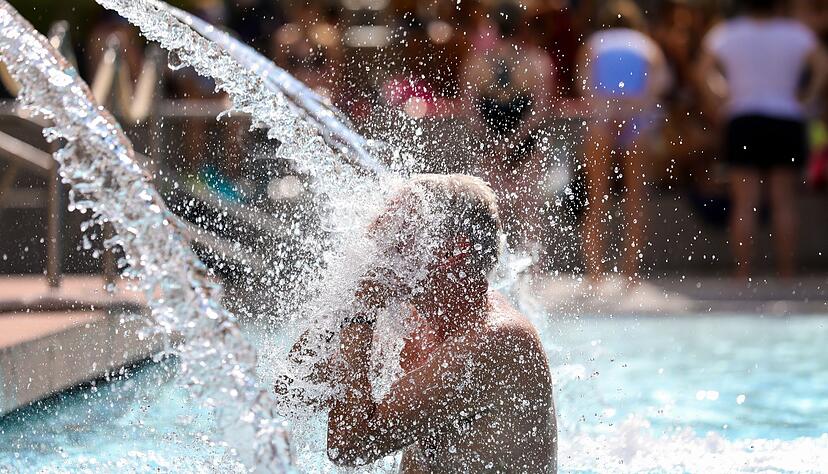 Ein Mann erfrischt sich im Donaubad in Sigmaringen unter einer Wasserfontäne.