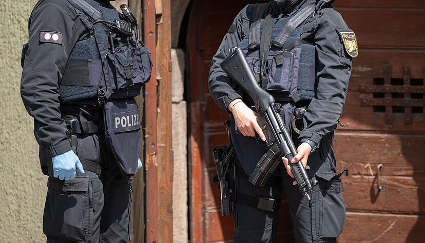 Eine Polizistin (r) steht mit einer Maschinenpistole vor einer Tür in Althengstett.
