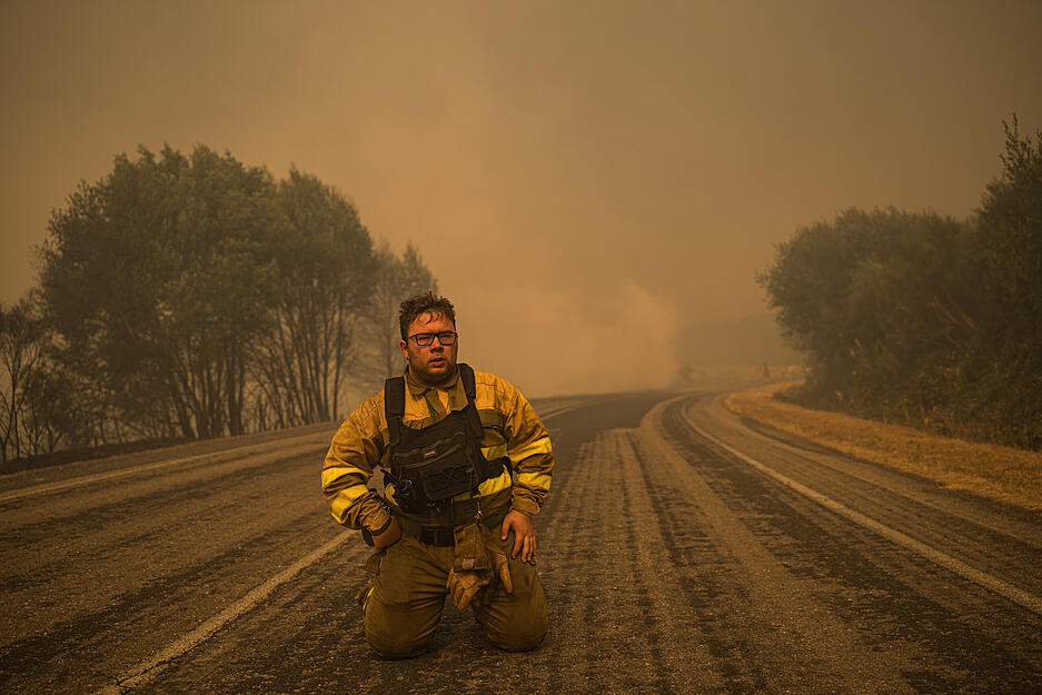 Ein Feuerwehrmann der Gemeindefeuerwehr von Cualedro in der Provinz Ourense, Galicien, kniet auf der Stra&szlig;e, nachdem sein Auto in Flammen aufgegangen ist.