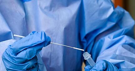 Eine Krankenschwester steckt ein Abstrichstäbchen in die Flüssigkeit eines Corona-Schnelltests.
