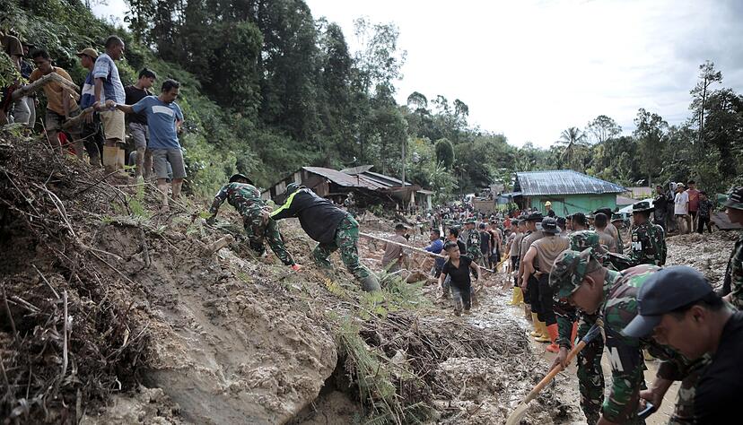 Rettungskr&auml;fte und Dorfbewohner beseitigen Schlamm.