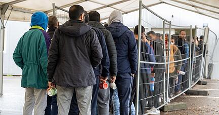Flüchtlinge warten in einer Landeserstaufnahmestelle in einer Schlange. Der Landkreistag spricht sich für die Prüfung von Asylanträgen an den EU-Außengrenzen und die Beendigung freiwilliger Aufnahmeprogramme aus.