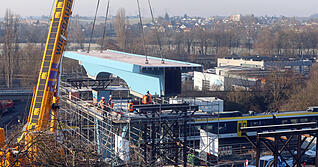 Ein gro&szlig;er Kran hat das erste Br&uuml;ckenteil am neuen Stadtbahnhalt "Kochendorf S&uuml;d" eingehoben. Die Br&uuml;cke f&uuml;hrt k&uuml;nftig auf den Schwarz-Digits-Campus.