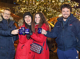 Besucher des Weihnachtsmarktes stoßen mit Heißgetränken auf die Eröffnung an.