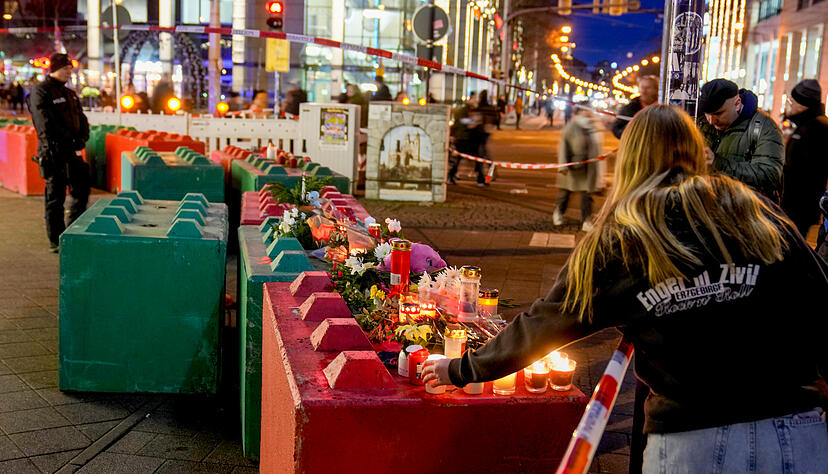 Menschen legen Blumen nieder und zünden Kerzen auf Betonblöcken an, die den Weihnachtsmarkt in Magdeburg schützen sollen. Menschen legen Blumen nieder und zünden Kerzen auf Betonblöcken an, die den Weihnachtsmarkt in Magdeburg schützen sollen.