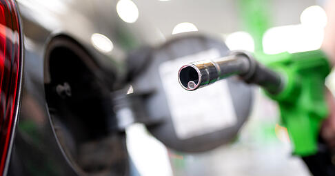 Eine Frau hält an einer Tankstelle an einer Zapfsäule eine Zapfpistole in der Hand und betankt ein Auto.