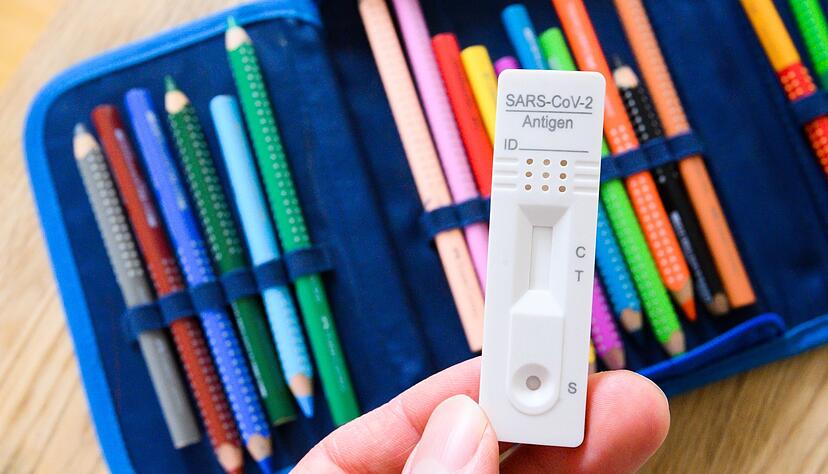 Ein Corona-Selbsttest wird über dem Federmäppchen eines Grundschülers gehalten. Ein Corona-Selbsttest wird über dem Federmäppchen eines Grundschülers gehalten.