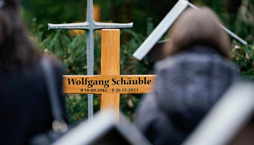 Trauergäste stehen auf dem Friedhof nach dem Trauergottesdienst für Wolfgang Schäuble (CDU) vor dem Holzkreuz mit der Aufschrift „Wolfgang Schäuble“.
