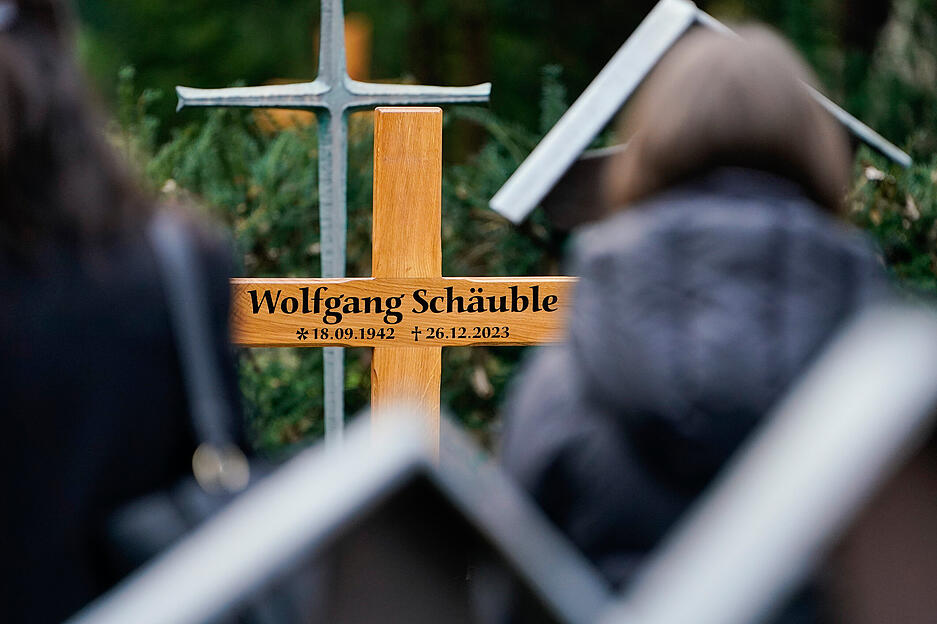 Trauergäste stehen auf dem Friedhof nach dem Trauergottesdienst für Wolfgang Schäuble (CDU) vor dem Holzkreuz mit der Aufschrift „Wolfgang Schäuble“.