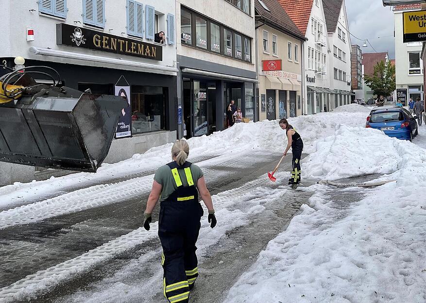Einsatzkräfte der Feuerwehr räumen Hagel von einer Straße.