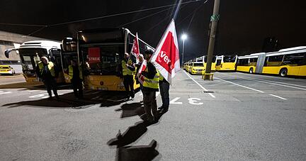 Teilnehmerinnen und Teilnehmer eines Warnstreiks stehen in einem Busdepot.