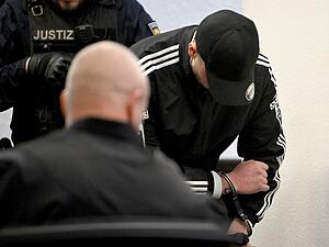 Einer der Angeklagten kommt im Landgericht in Handschellen zum Prozess wegen Mordes an zwei jungen Frauen nach einem Autorennen.