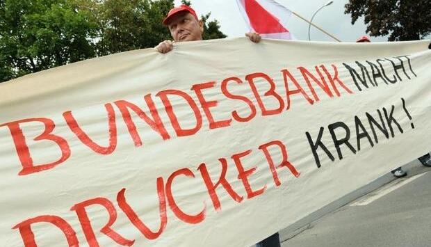 Ein Gelddrucker demonstriert vor der Deutschen Bundesbank in Frankfurt am Main mit einem Transparent.