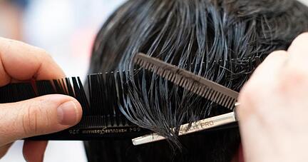 Ein Friseur schneidet einer Kundin mit einer Schere die Haare in einem Friseur-Salon.