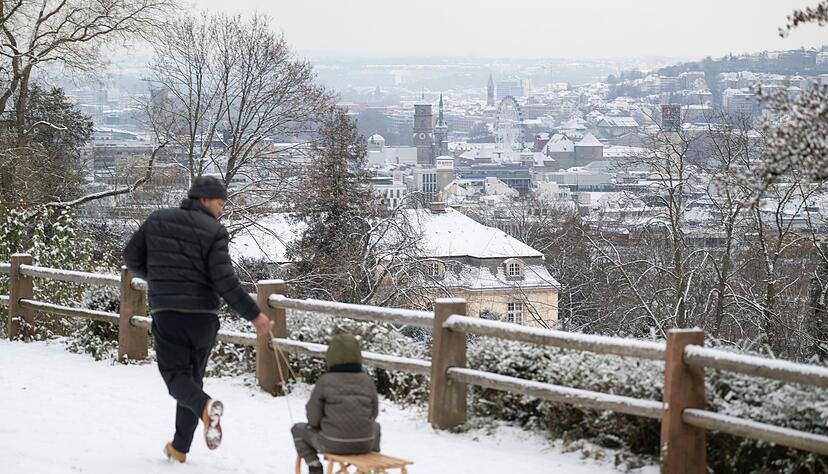 Es schneit: Ein Mann zieht seinen Sohn auf einem Schlitten, im Hintergrund ist das Stuttgarter Stadtzentrum sehen.