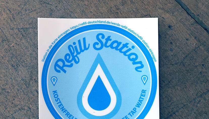 Ein blauer Aufkleber mit einem Wassertropfen am Eingang signalisiert, dass es sich um eine Refill-Station handelt.