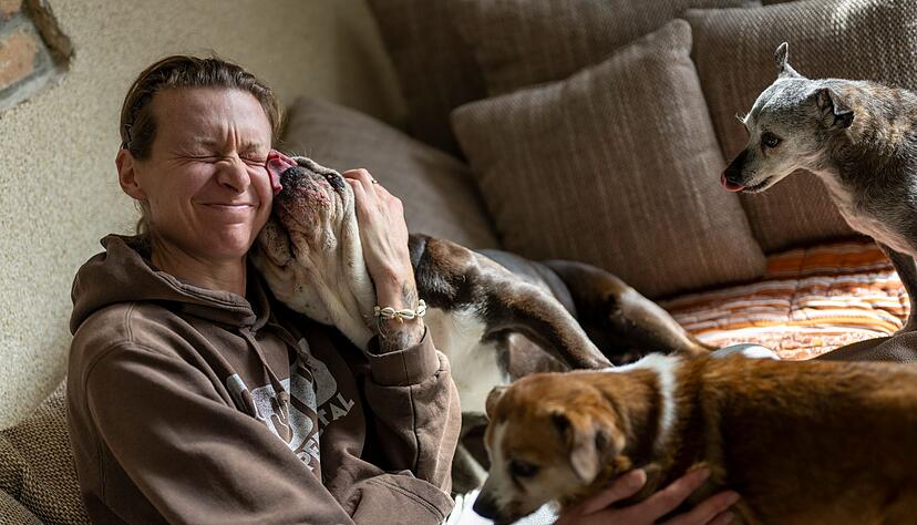 Stephanie Badura sitzt auf dem Sofa in ihrem Wohnzimmer und kuschelt mit ihren Pflegehunden.