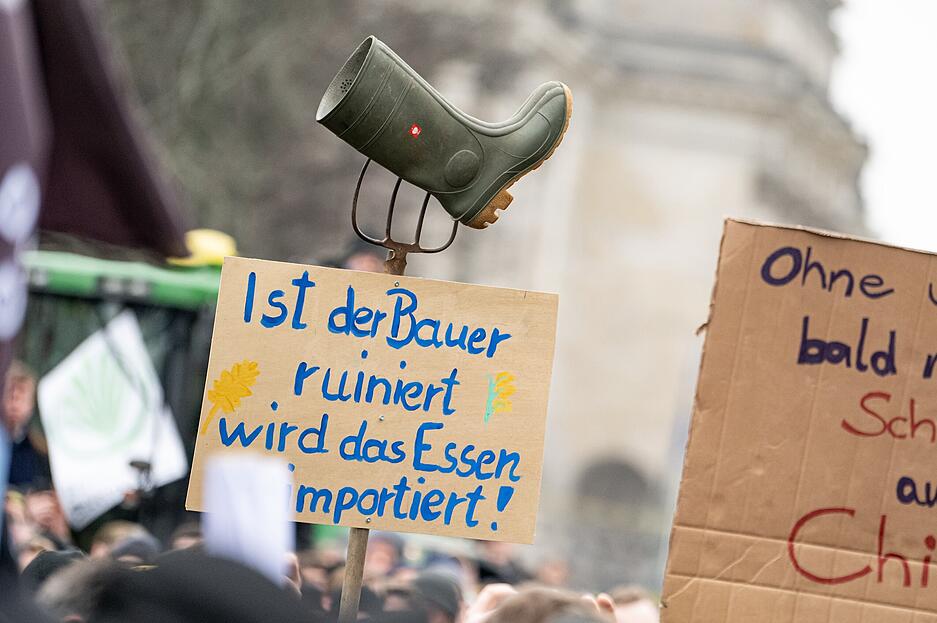 Vor dem Brandenburger Tor hält jemand ein Schild mit der Aufschrift „Ist der Bauer ruiniert wird das Essen importiert“ mit eine Mistgabel und einem Gummistiefel hoch.
