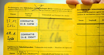 Eine Person hält einen gelben Impfpass mit den Aufklebern vom Biontech Pfizer-Impfstoff. Foto: dpa