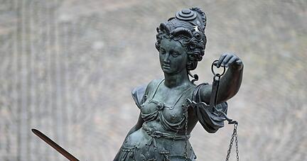 Eine Statue der Justitia hält eine Waage und ein Schwert in der Hand.
