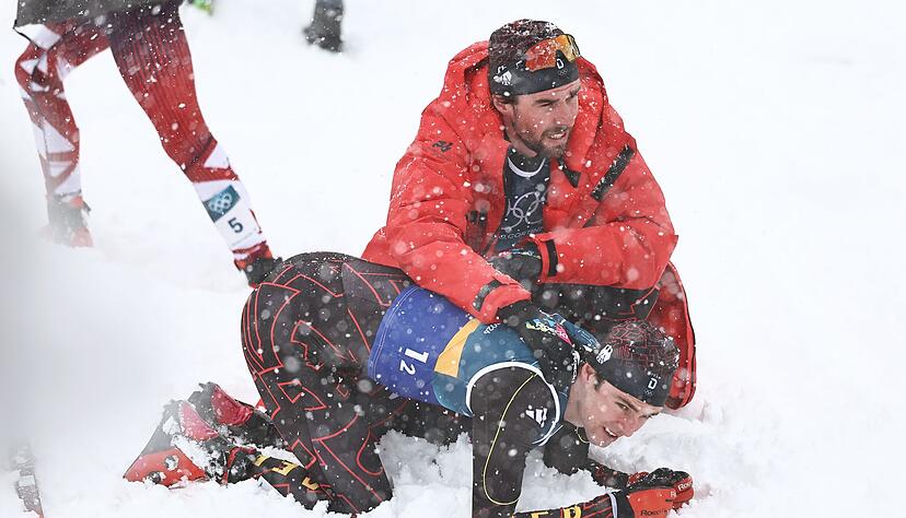Vinzenz Geiger liegt im Schnee und wird von Teamkollege Johannes Rydzek getr&ouml;stet.