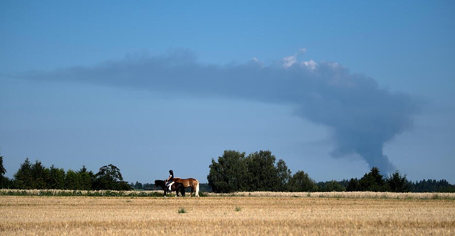 Eine Frau reitet &uuml;ber ein Feld, w&auml;hrend im Hintergrund die Rauchs&auml;ule des Gro&szlig;brandes im rund 20 Kilometer entfernten Remseck aufsteigt.