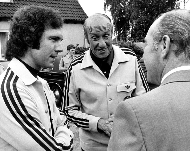 Der damalige Bundestrainer Helmut Schön (M) und damalige Kapitän Franz Beckenbauer (l) im Gespräch mit einem Journalisten im WM-Trainingslager der deutschen Fußballnationalmannschaft in der Sportschule bei Kamen.