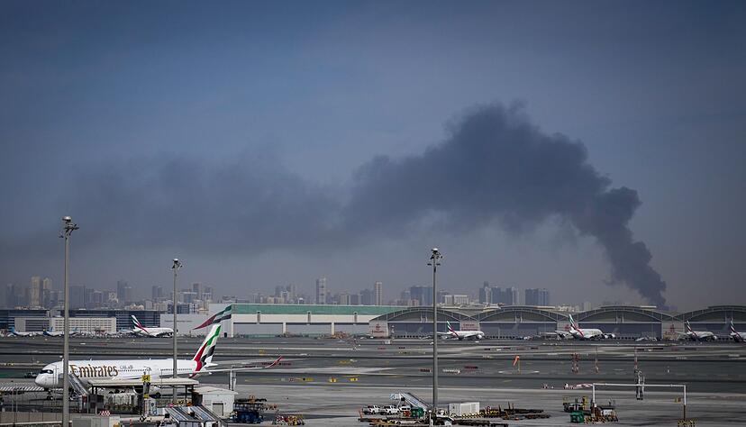 Eine Rauchwolke im Hintergrund, w&auml;hrend Flugzeuge auf dem geschlossenen Dubai International Airport geparkt sind.