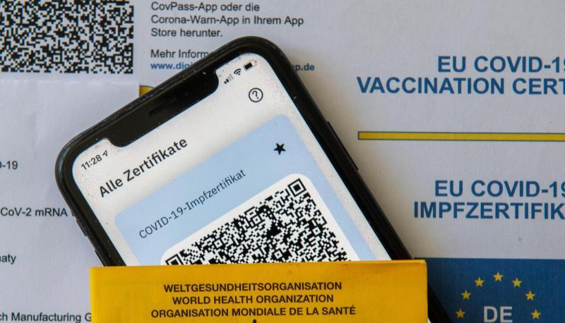 Ein Impfpass und ein Smartphone mit der CovPass-App liegen auf einem Impfzertifikat.